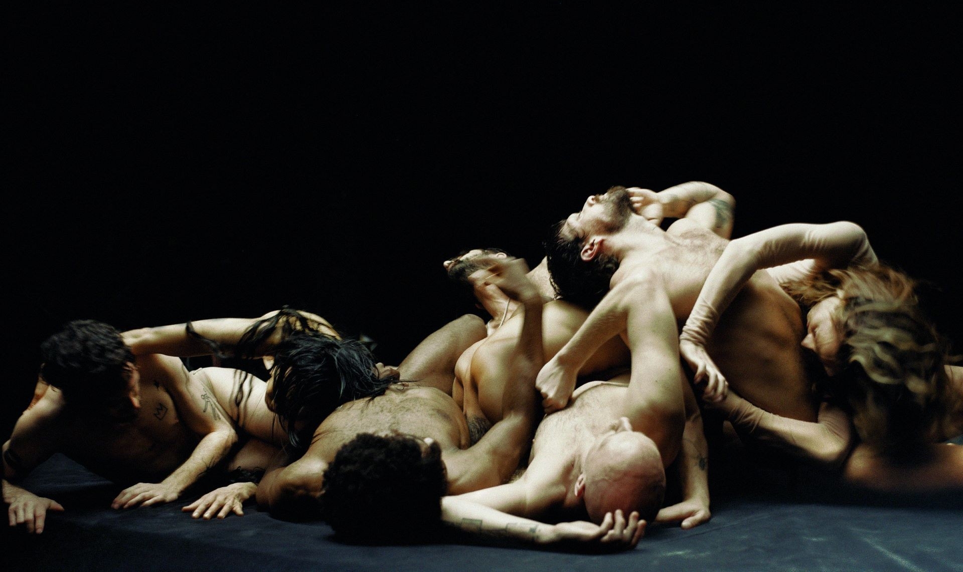 Heap of dancers' bodies with limbs draped over one another, against a black background