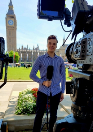 Bogdan stands in front of a camera with a microphone in hand.