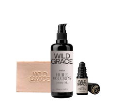 A pink soap bar, a large bottle of body oil and a small bottle perfume by the brand Wild Grace appear in front of a white background