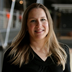 Portrait of a smiling woman with long hair. She is wearing a black v-neck top.