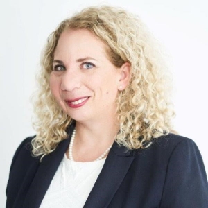 Portrait of a smiling woman with shoulder-length curly hair. She is wearing a business suit and a pearl necklace.