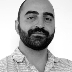 Black and white photo of a man with a dark beard who is wearing a patterned collared shirt.