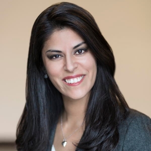 Portrait of a smiling woman with long, straight black hair. She is wearing a business suit and a pendant necklace.