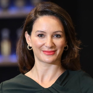 A woman with dark brown hair is wearing hoop earrings and a dark v-neck shirt.