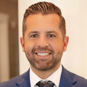 Portrait of a smiling, slightly bearded man in a suit and tie.