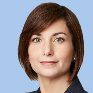 Portrait of an auburn-haired woman with a bob cut wearing a blazer and pearl earrings.