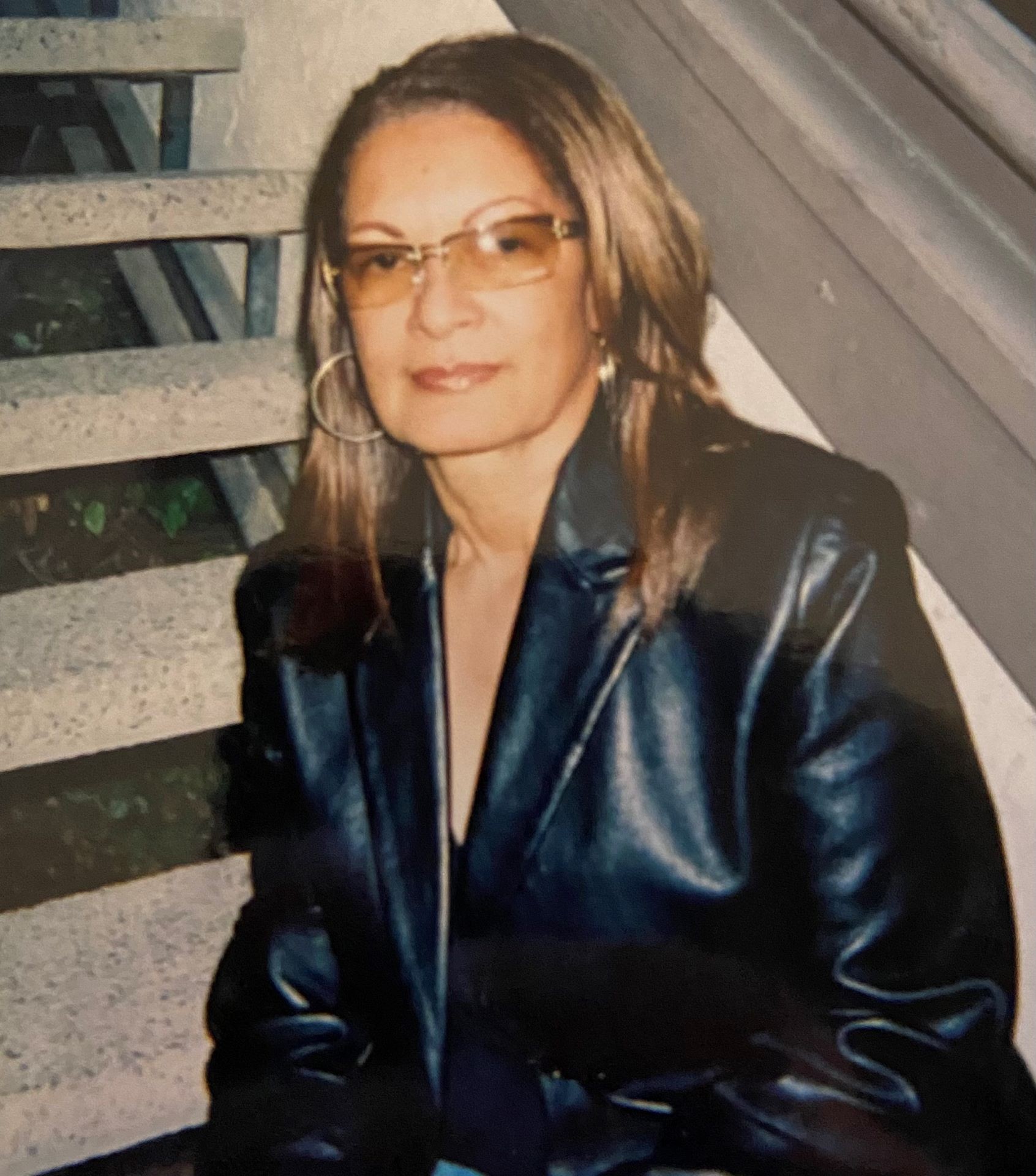 A woman wearing glasses sits on a staircase in a leather blazer