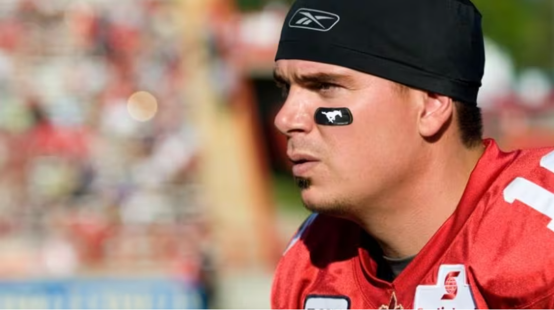  Focused football player with eye black, wearing a red jersey and a black cap, in a blurred stadium background.