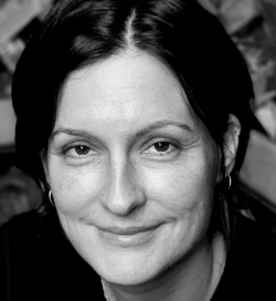 Black and white portrait of a smiling woman with shoulder-length hair, earrings, and a nose ring, looking slightly to the left.