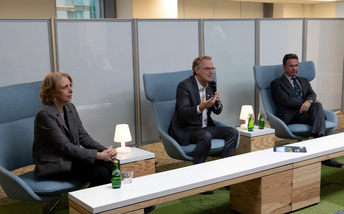 Three professionals are seated in blue chairs appear to be participating in a question and answer period.