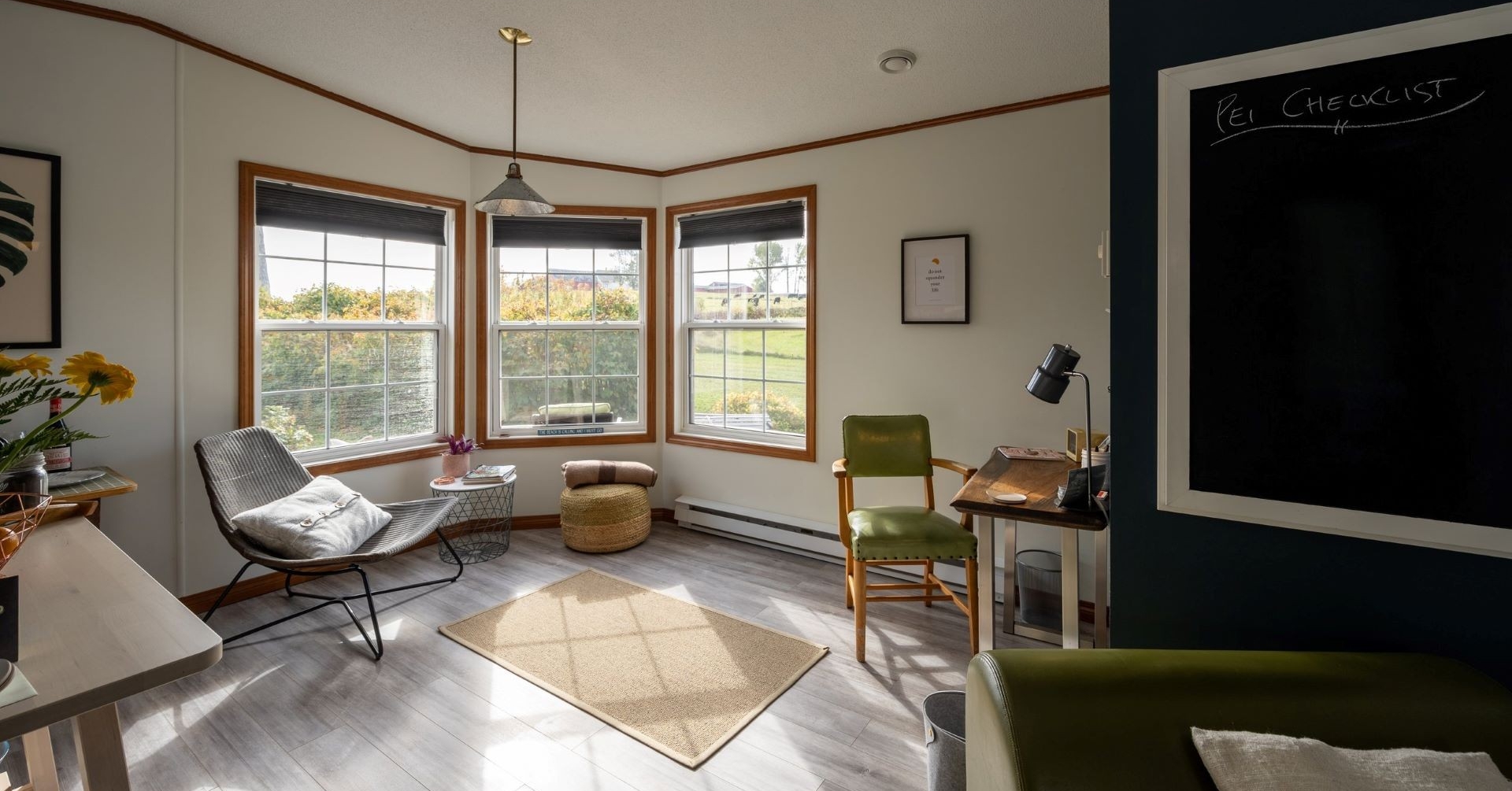 A sunny room with three large windows, small desk and two chairs, with a blackboard.  