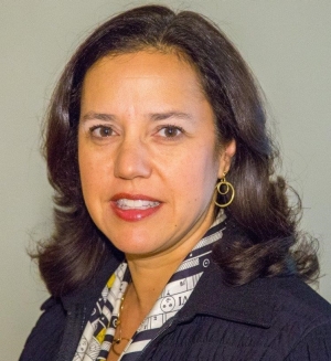 A woman with shoulder-length, brown hair wears circular gold earrings, a black jacket and a scarf.