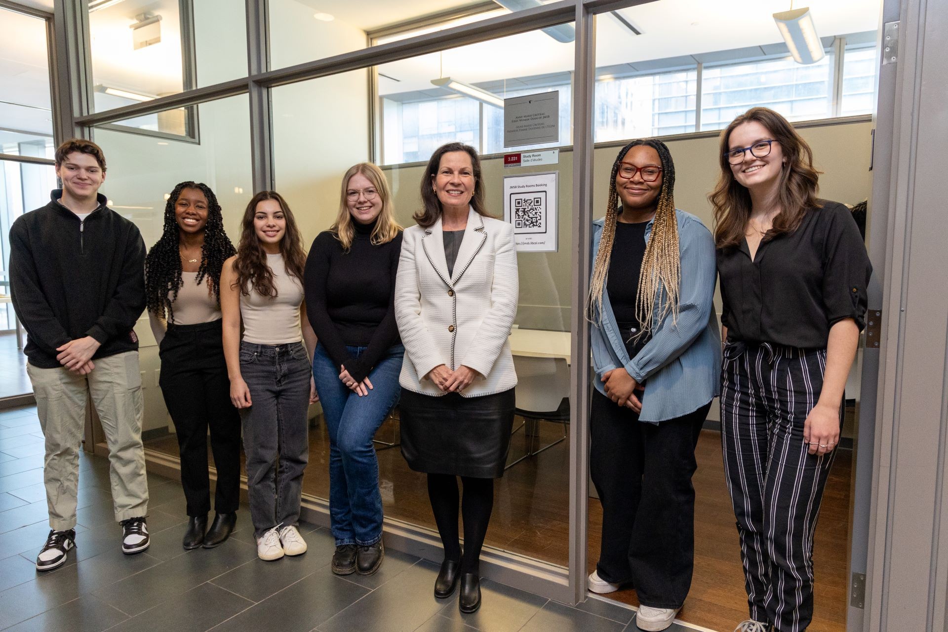 Anne-Marie Croteau has donated $55,000 to support women students at the John Molson School of Business. A smiling individual in professional attire poses alongside a group of five casually dressed people in a hallway with glass walls.