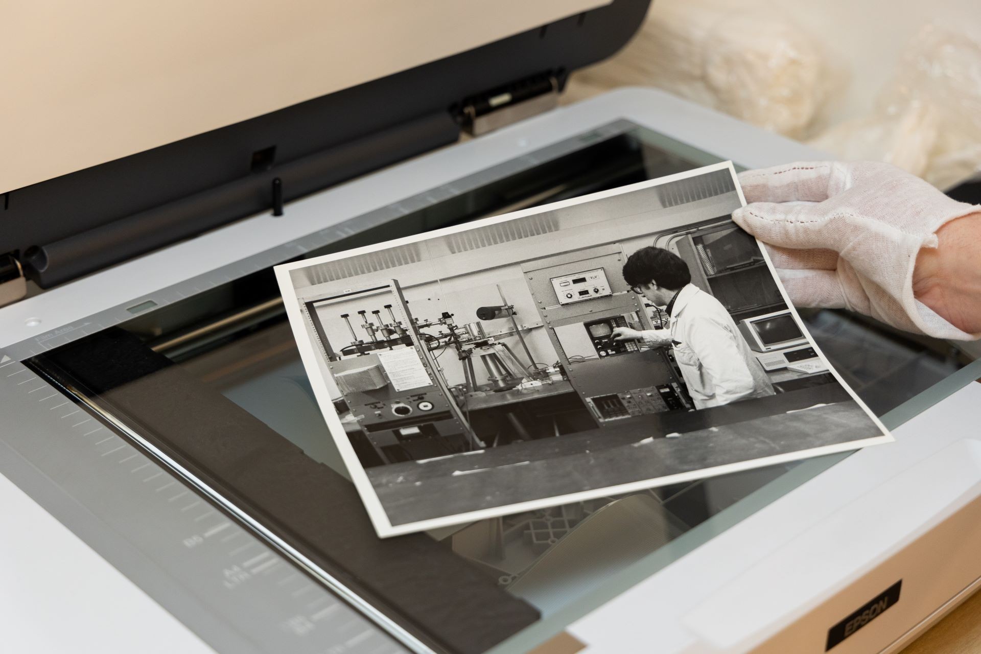 A white-gloved hand holds a black-and-white photo over a scanner.