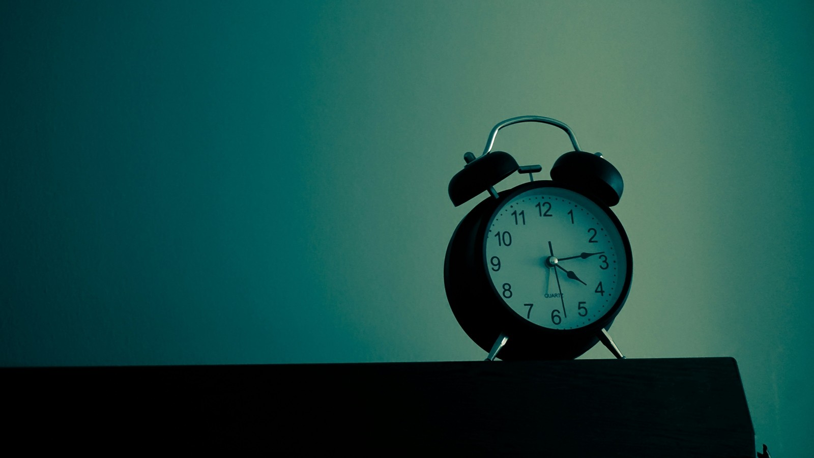 An analog alarm clock sits atop of a dresser. The image is overlaid with hues of green.