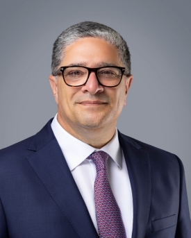 Portrait of a man wearing dark-rimmed glasses, a dark suit, white shirt and dark-colored tie