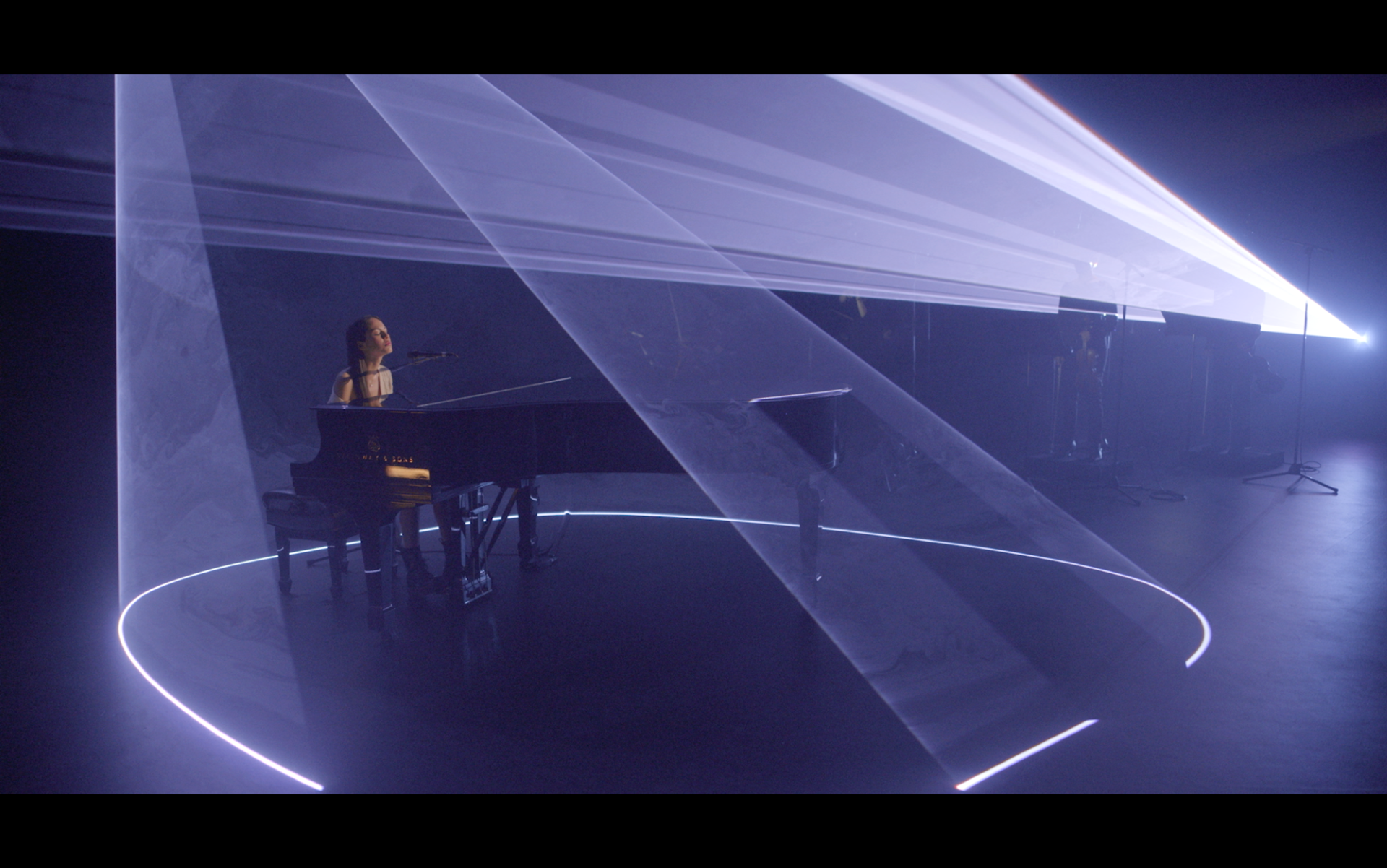 Female performing at a piano surrounded by dramatic stage lighting.