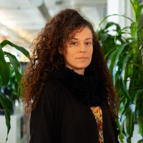 Portrait of Pamela Schneider with curly hair standing in an office environment.
