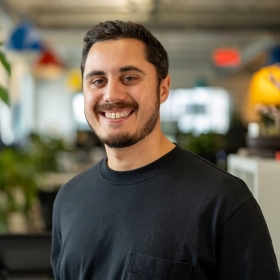 A man smiling in a casual office setting with indoor plants.