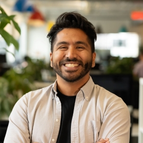 A man in a light grey shirt, smiling confidently in a creative workspace