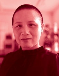They have short, buzzed, dark hair and wear a mock-neck, dark top. They look directly into the camera.