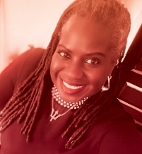A close up of woman with long black braids and a black shirt smiling to the camera.