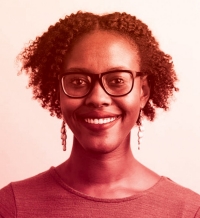 A woman with short black hair and black-framed glasses is wearing a green top and dangling earrings. She is smiling and is posing in front of a light grey background