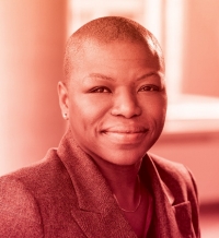A woman in a grey blazer is pictured with a large window behind her