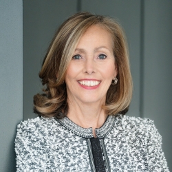 Woman with shoulder length hair smiles for the camera in a grey and white jacket
