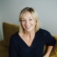 A woman with blonde hair wearing a black shirt sits smiling for a portrait.