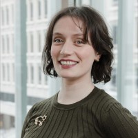 A woman with brown hair wearing a green sweater sits smiling for a portrait.