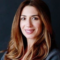 A woman with long dark hair wearing a grey jacket sits smiling for a portrait.