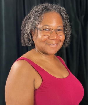 Woman in a pink tank top and grey and black curly hair smiles into the camera.