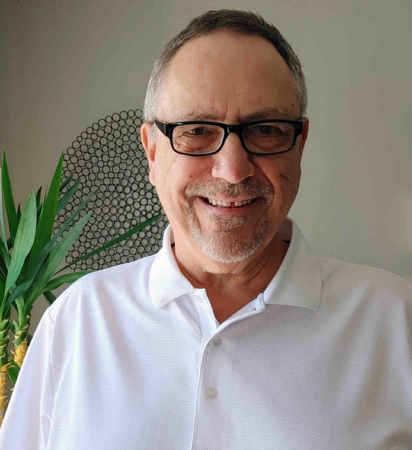 A man wearing glasses and a white polo shirt smiles at the camera