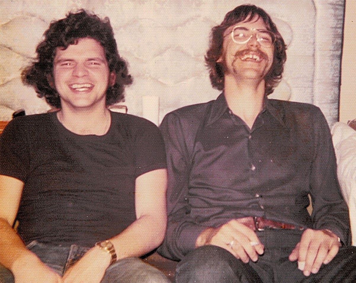 Two men with brown hair, wearing black shirts, share a hearty laugh