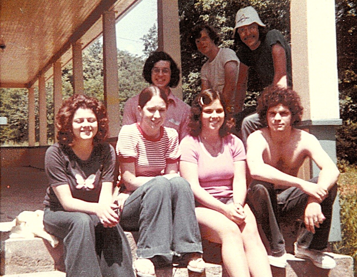 A group of six people sit on the steps outside a building with trees in the background