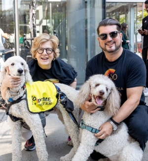 Two individuals pose next to white poodles.