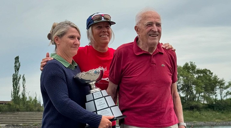 A woman holds a trophy next to another woman and an older man