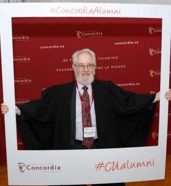 A man with white hair, beard and glasses poses with a large white frame that says "Concordia Alumni"