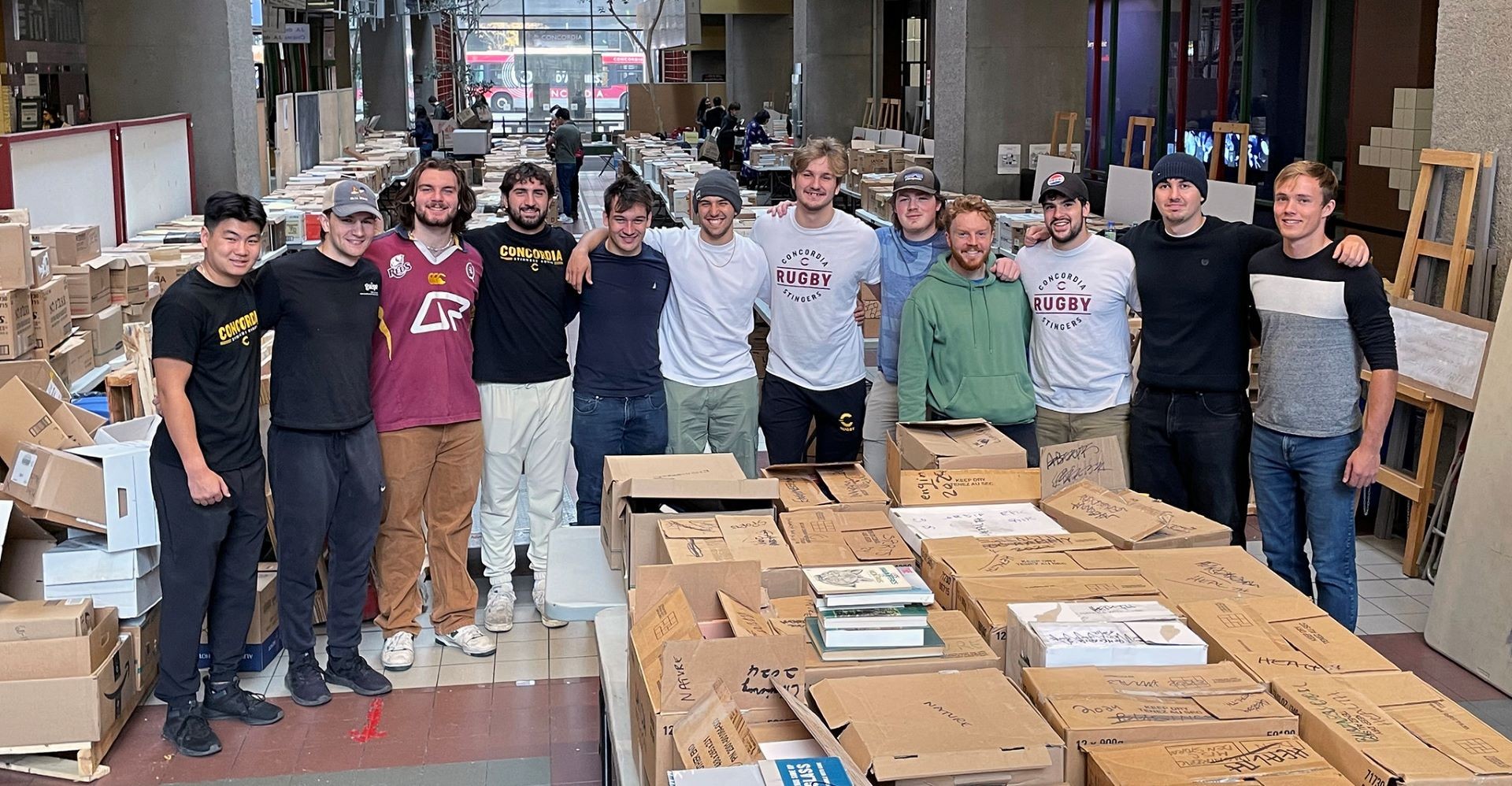 A group of men stand side by side, surrounded by boxes filled with books
