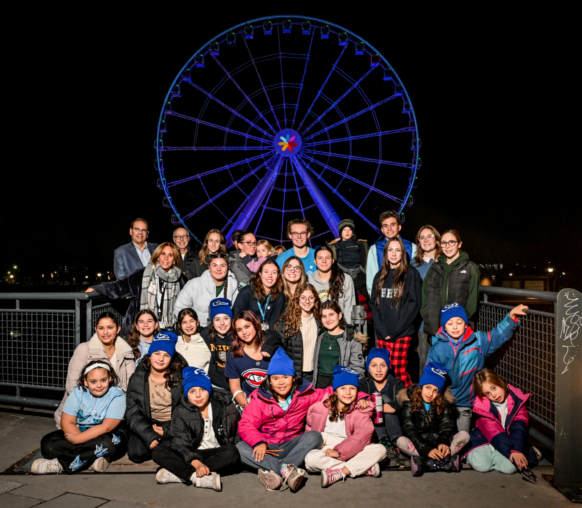 Children’s Grief Awareness Day A group of children adults pose as a group in from of a large ferris wheel that is lit up in blue lights.