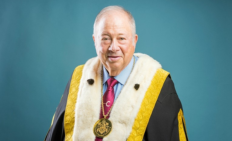 Portrait of a man wearing navy chancellor's robes decorated with gold fabric trim and white fur