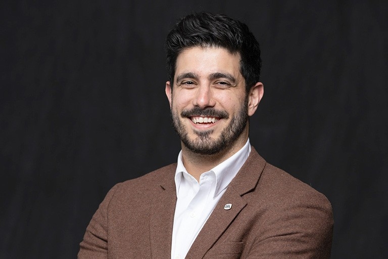 Eric Noivo A young man with short dark hair wears a white shirt under a browm tweed jacket. He has a CFL pin on his lapel.