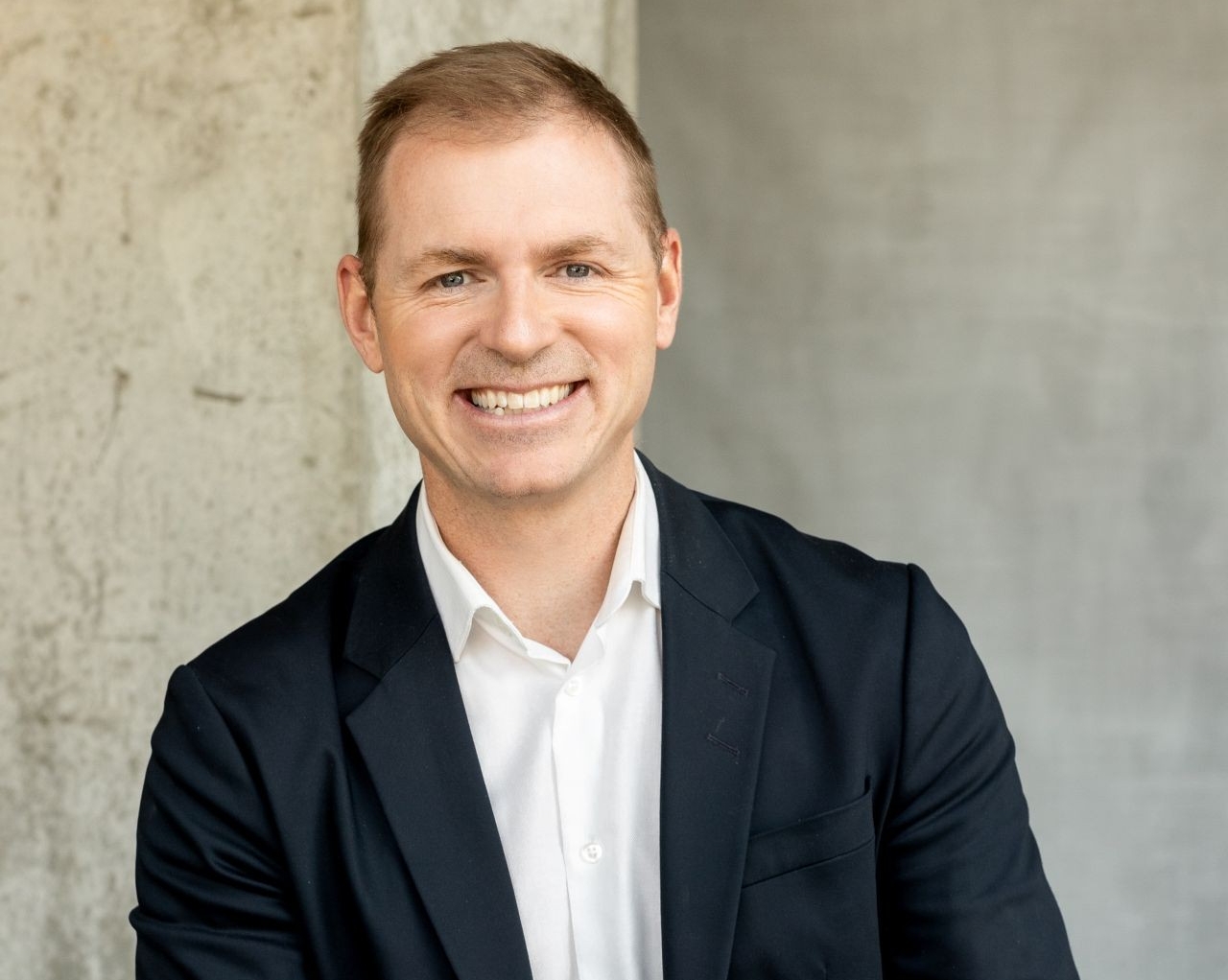 Hugo Germain A male wearing a navy blue blazer and white collared shirt stands smiling.