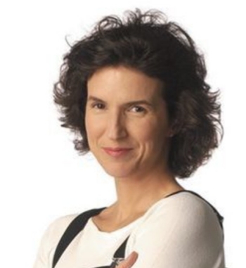 A smiling individual with short, curly hair wearing a light-colored top, posed confidently against a white background.