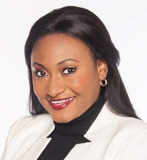 A smiling individual with long, straight hair wearing a light-colored blazer and black top, posed warmly against a white background.