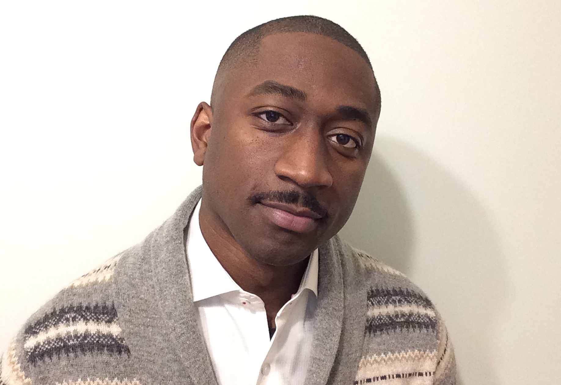 A man with short black hair wearing a white shirt and button up sweater.