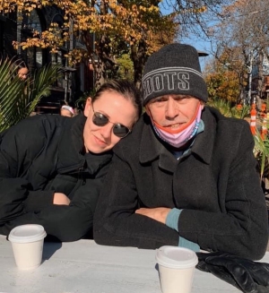A woman and man sit outside in the sun on a cold day with takeout coffee cups in front of them