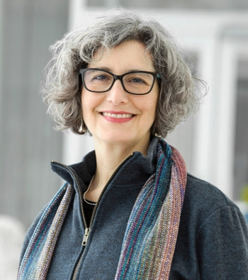 alt="woman with short hair and glasses looks at the camera."