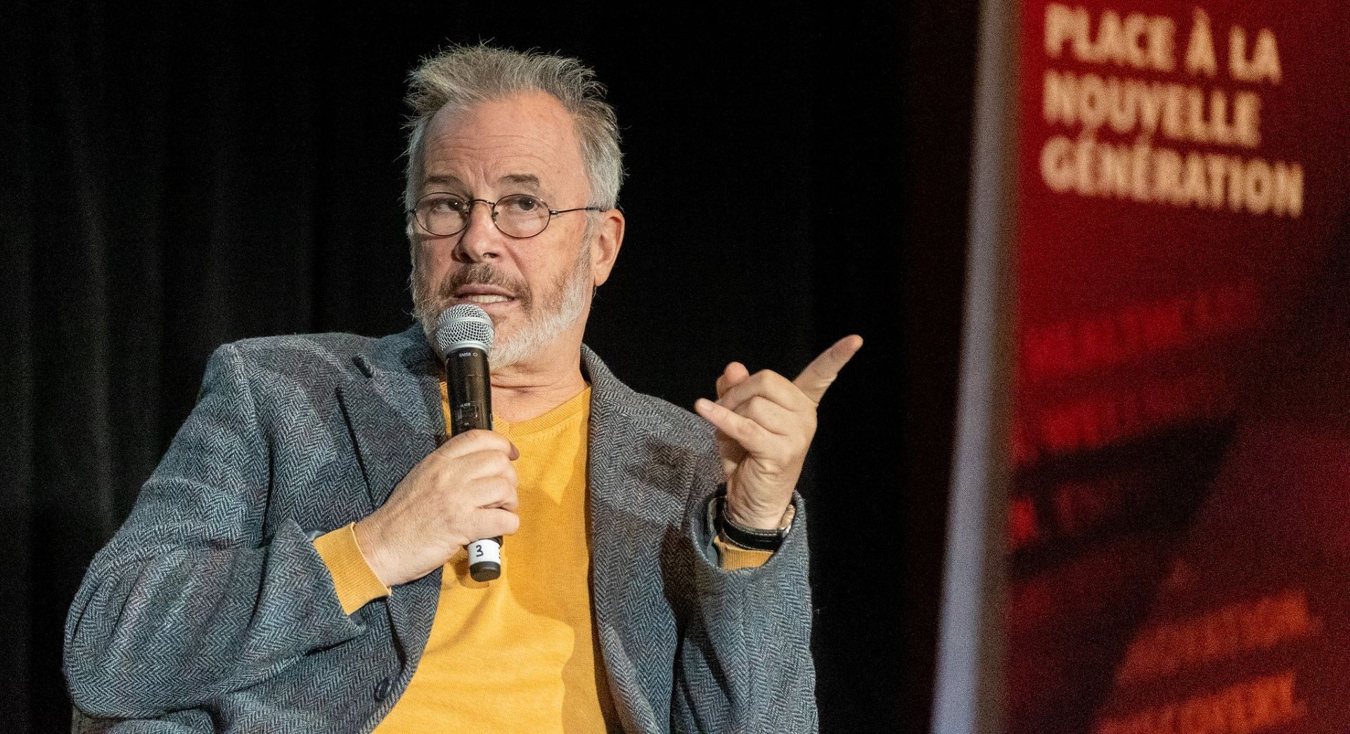 A man with gray hair and beard holds a microphone